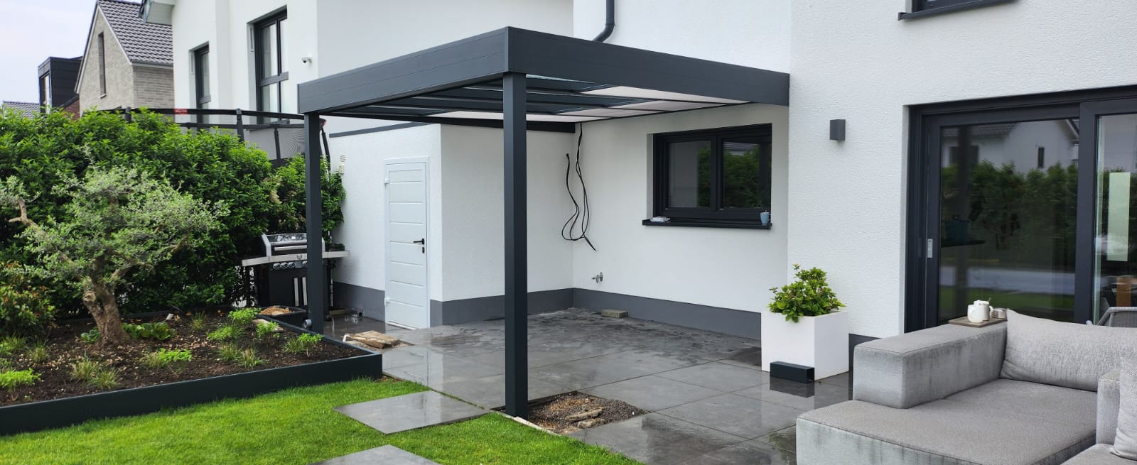 Terrassenüberdachung mit schwarzem Rahmen und Sitzbereich