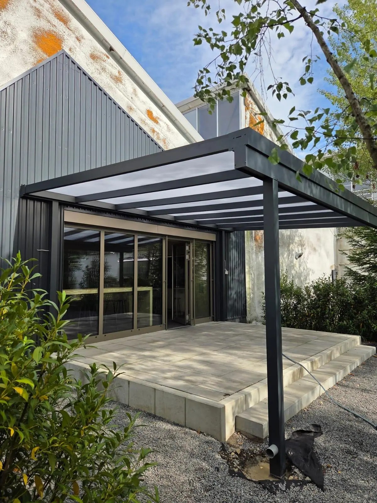 Pultdach mit Polycarbonat-Eindeckung in Opal, schräg von vorn mit gepflasterter Terrasse