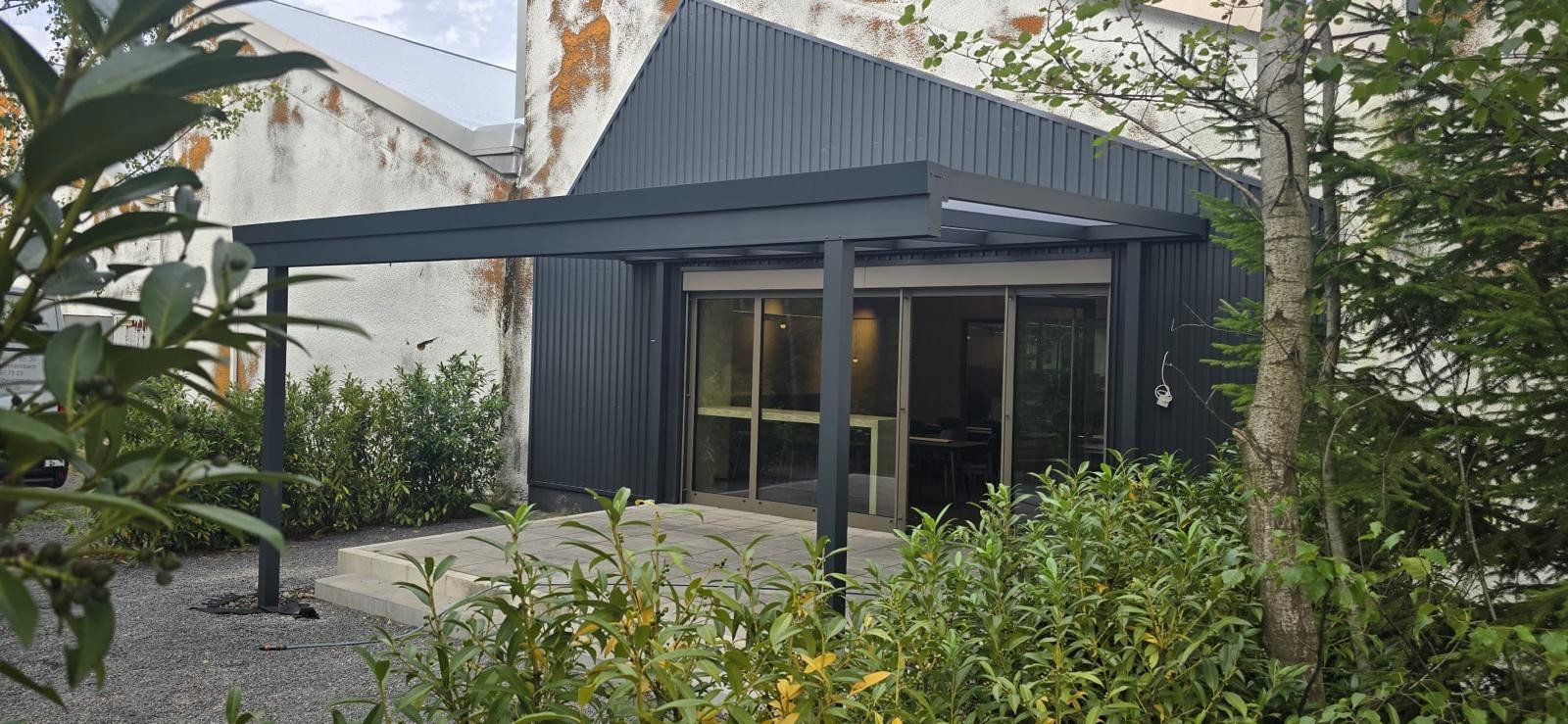 Terrassendach mit Pultdach und opalen Polycarbonat-Platten, Ansicht von der Seite mit Bewuchs im Vordergrund